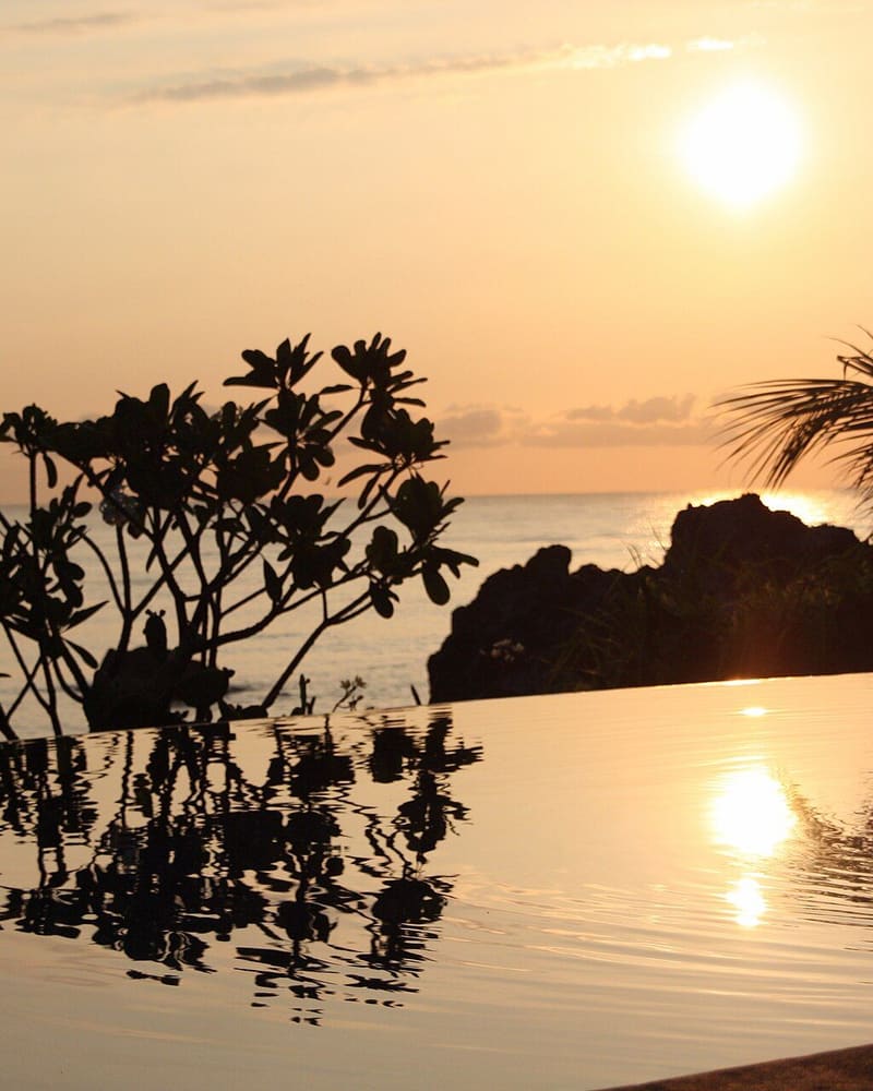 Infinity pool reflecting a warm sunset over the ocean in Bali