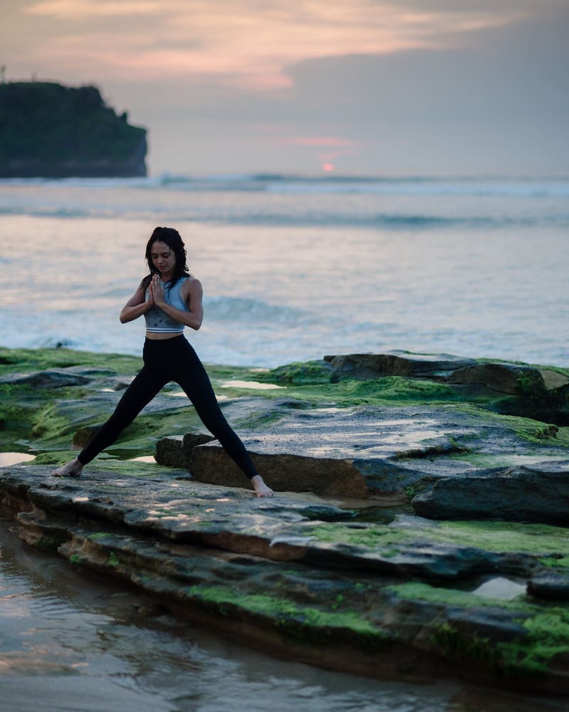 Woman practising yoga on rocks by the sea in Bali at sunset